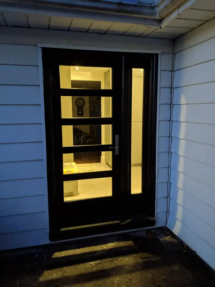 Modern black entry door with horizontal glass lites, lit up at dusk