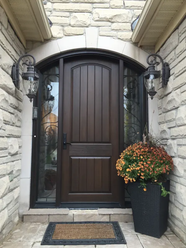 Stained fiberglass entry door with an arched frame, wrought-iron glass sidelites and lanterns