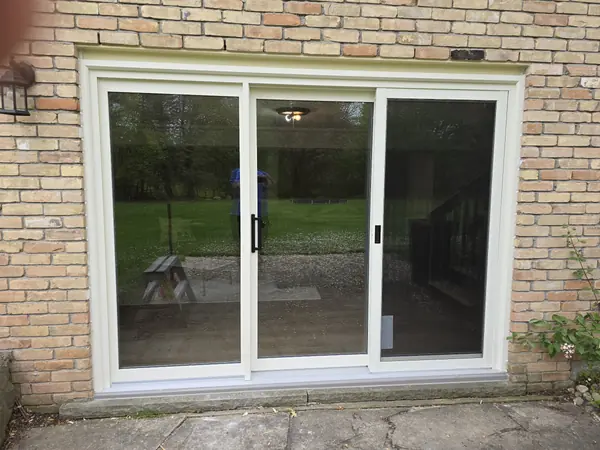 White three-panel sliding patio door in a tan brick wall