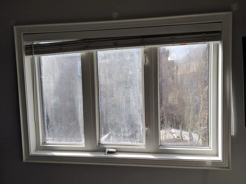 Before glass replacement: white three-panel casement window with heavy fog between the panes