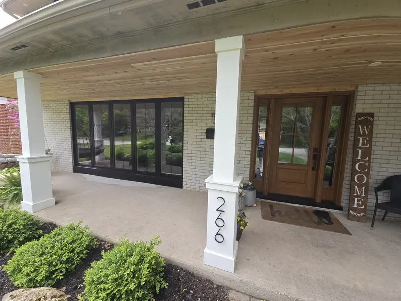Front porch of a Burlington-area home with new black-frame windows and a stained front door