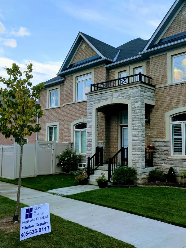 Tan brick and stone home with a Glass by Derrick lawn sign for foggy and cracked window repairs